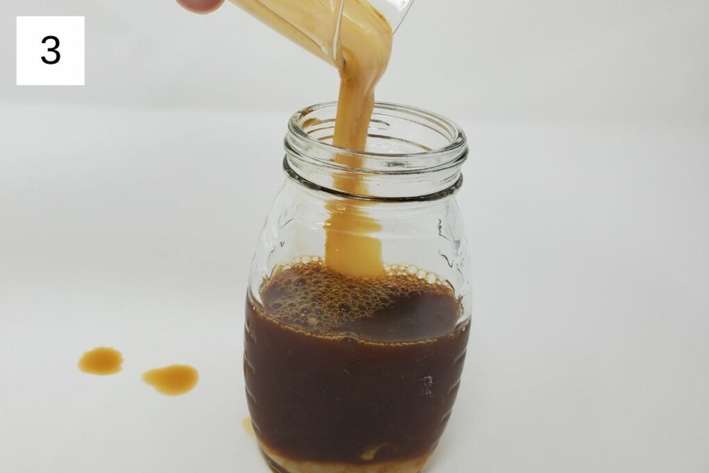 pouring yuzu syrup and condensed milk into a glass container of brewed espresso