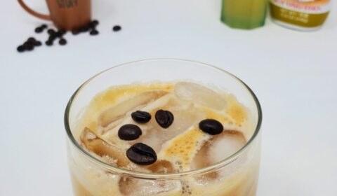 iced yuzu coffee mixture in a glass topped with raw coffee beans.