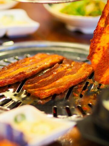 A table with a Korean barbecue grill and different side dishes.