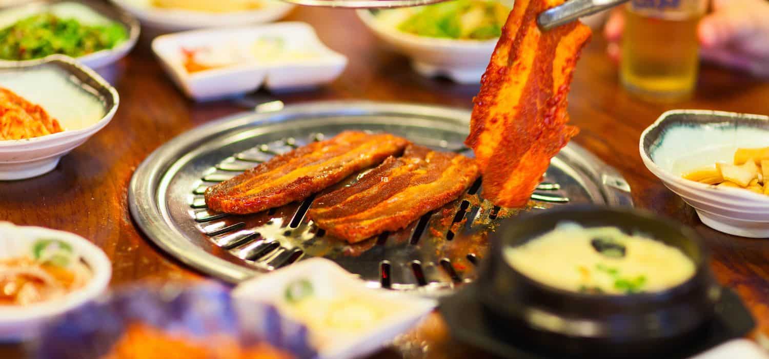 A table with a Korean barbecue grill and different side dishes.