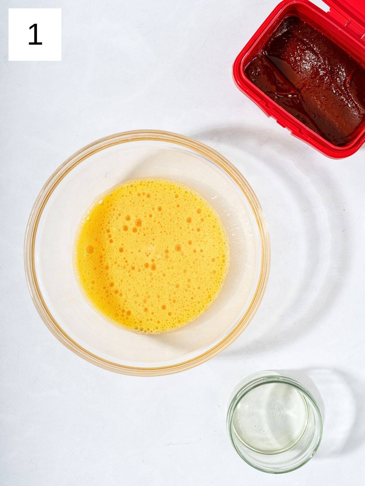 A bowl of scrambled eggs next to oil and gochujang paste.