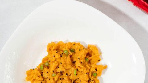 A serving of gochujang eggs topped with green onions and sesame seeds in a plate next to gochujang paste.