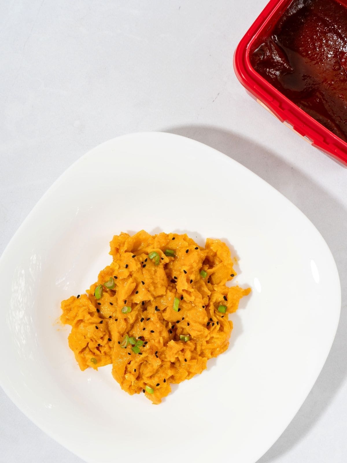 A serving of gochujang eggs topped with green onions and sesame seeds in a plate next to gochujang paste.