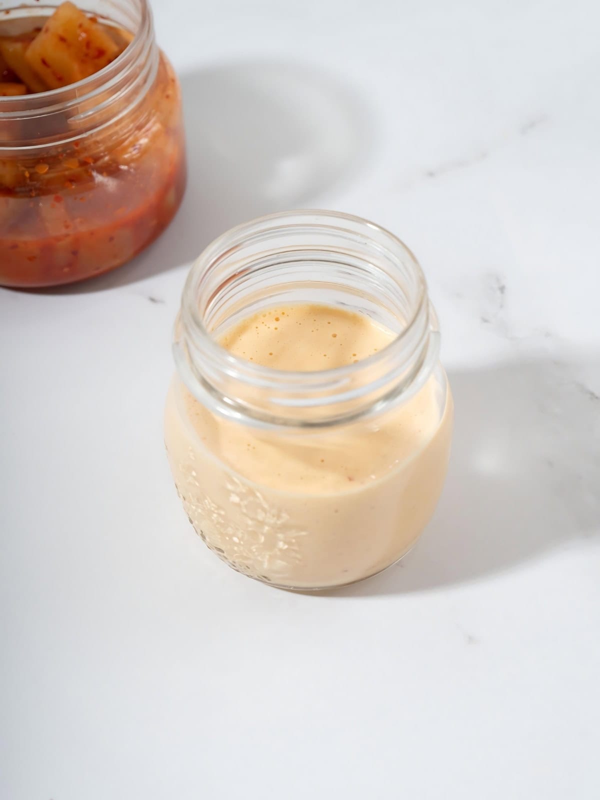 Kimchi aioli in a jar next to kimchi.