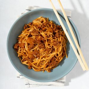 A bowl of kimchi noodles mixed with ground meat and kimchi next to chopsticks.
