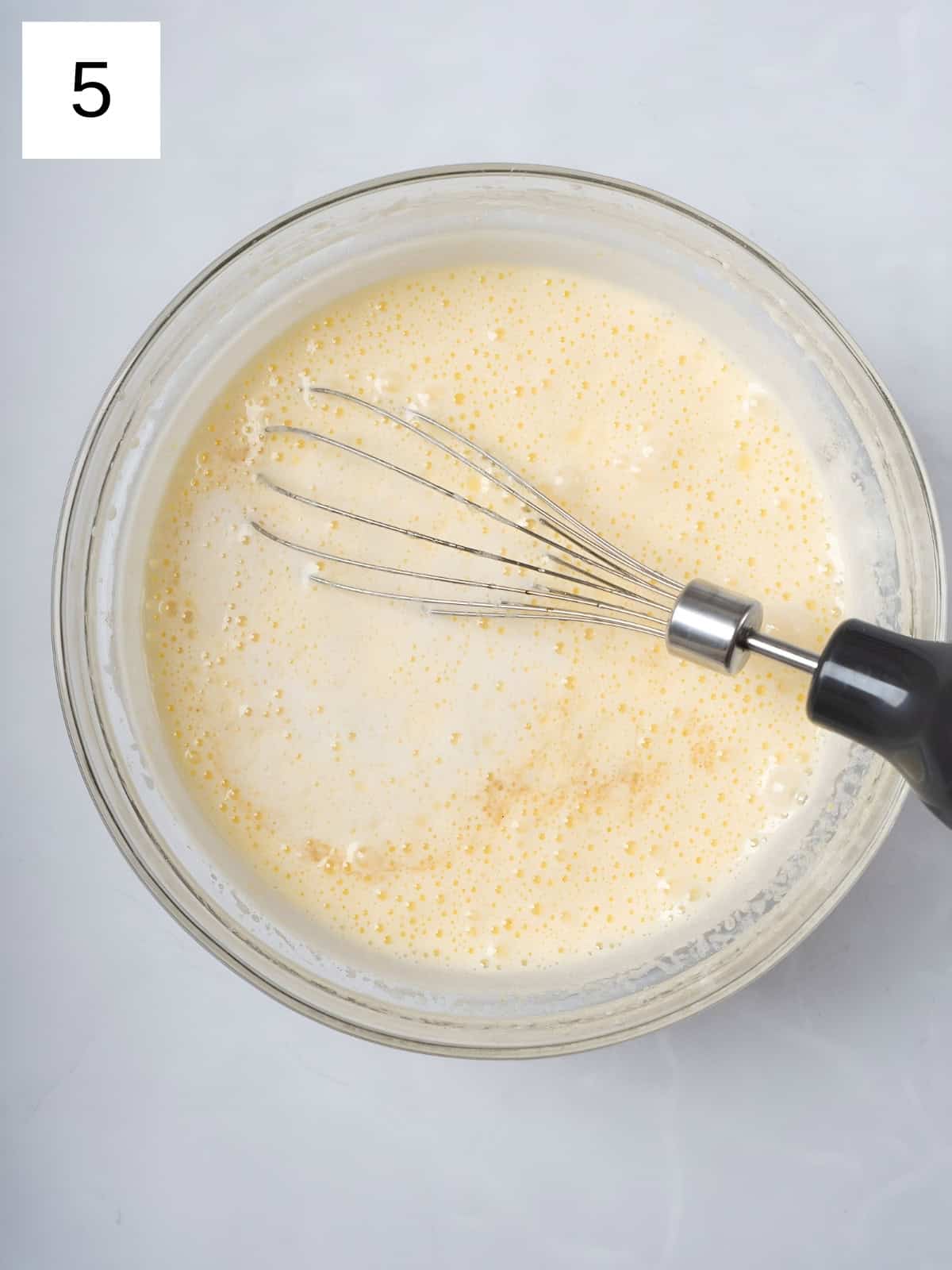 Egg and sugar mixture with added butter and vanilla extract being whisked in a bowl.