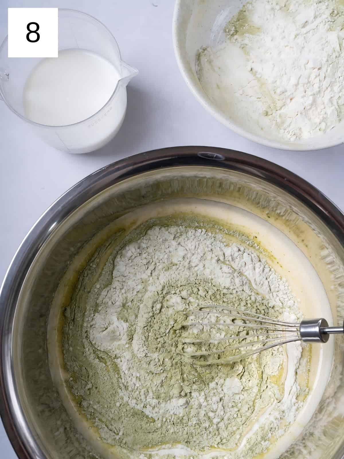 Egg and matcha mixture with added flour being whisked, next to a bowl of flour and cream.