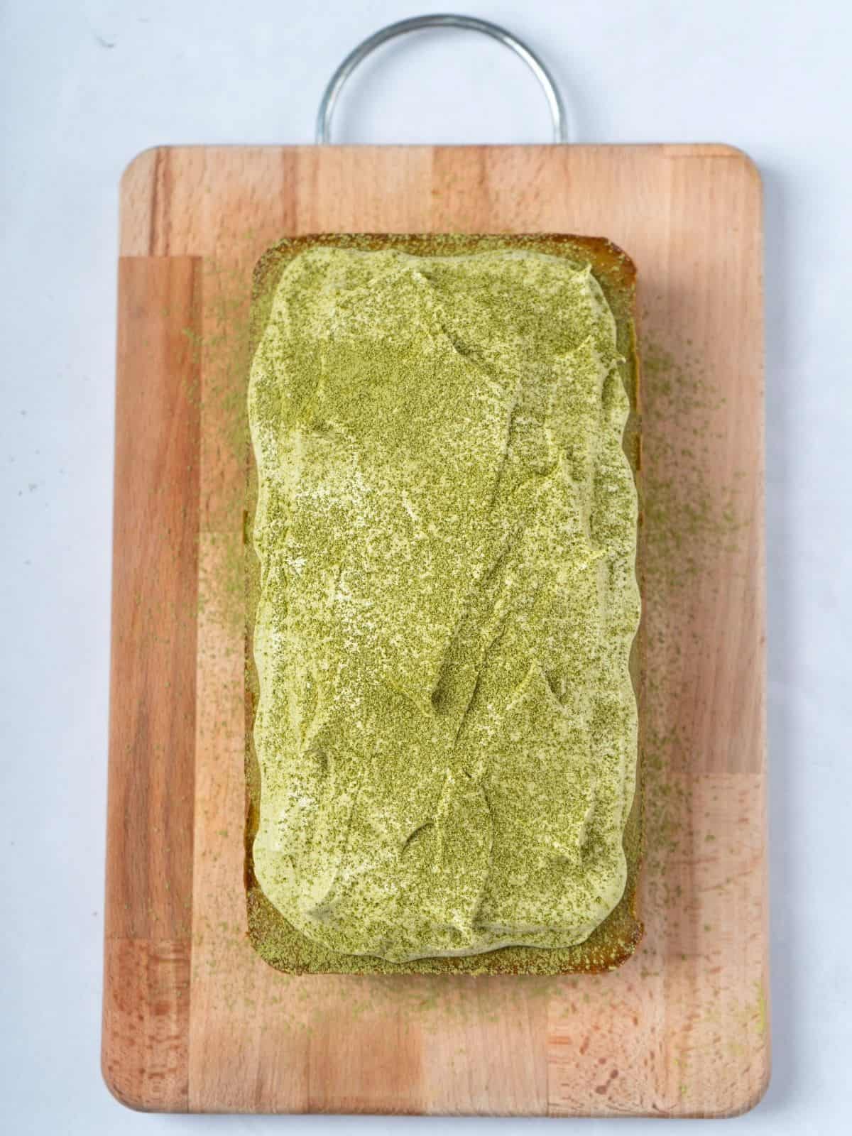 A matcha cake topped with matcha frosting and sprinkled with matcha powder.