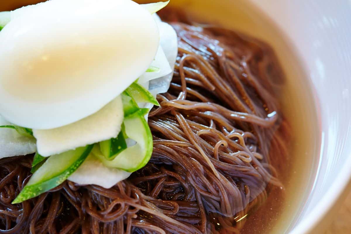 Nangmyeon served with poached egg and cucumbers on top.