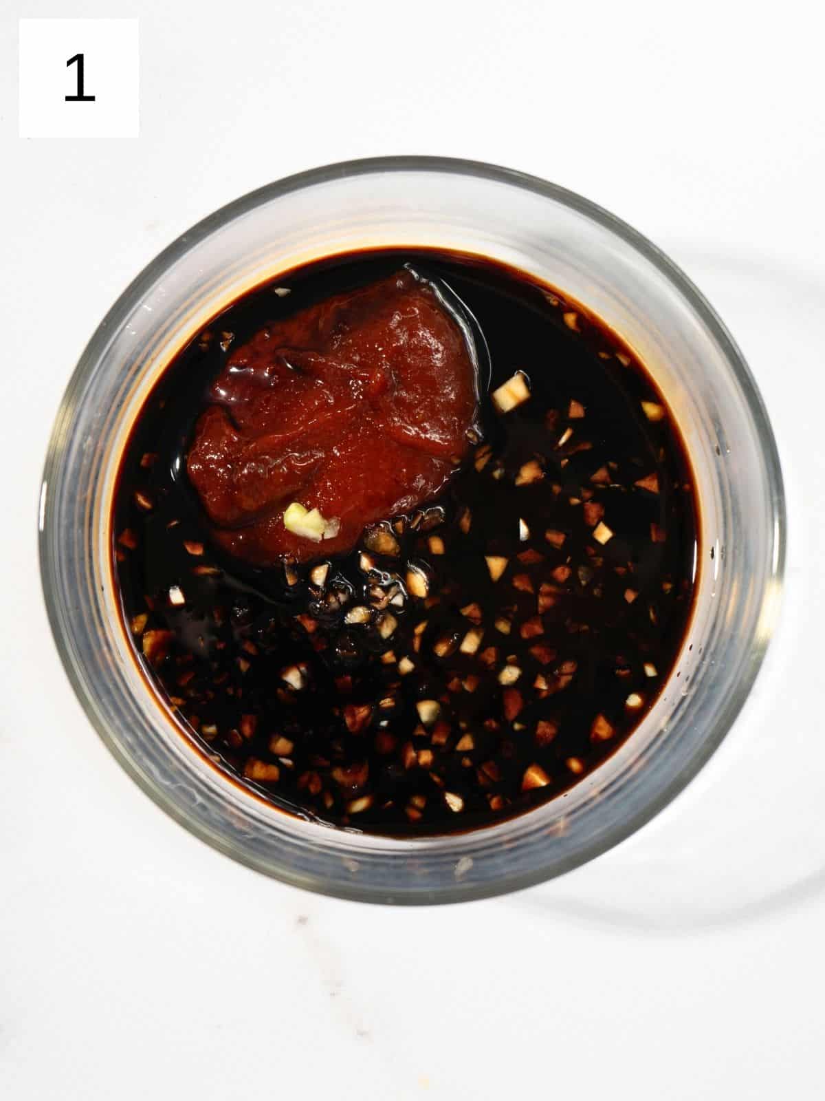 A bowl of soy sauce with gochujang and garlic.