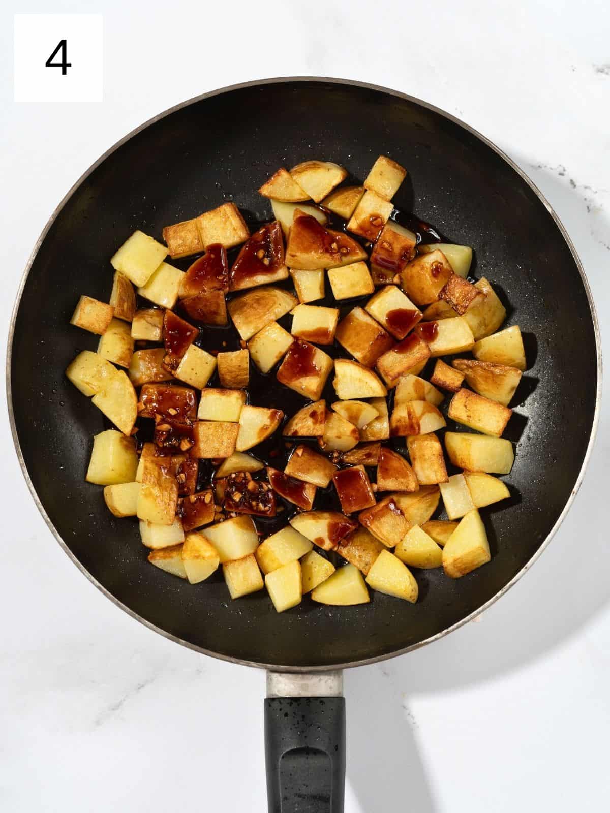 Soy sauce and gochujang mixture being poured over potato cuts in a pan.