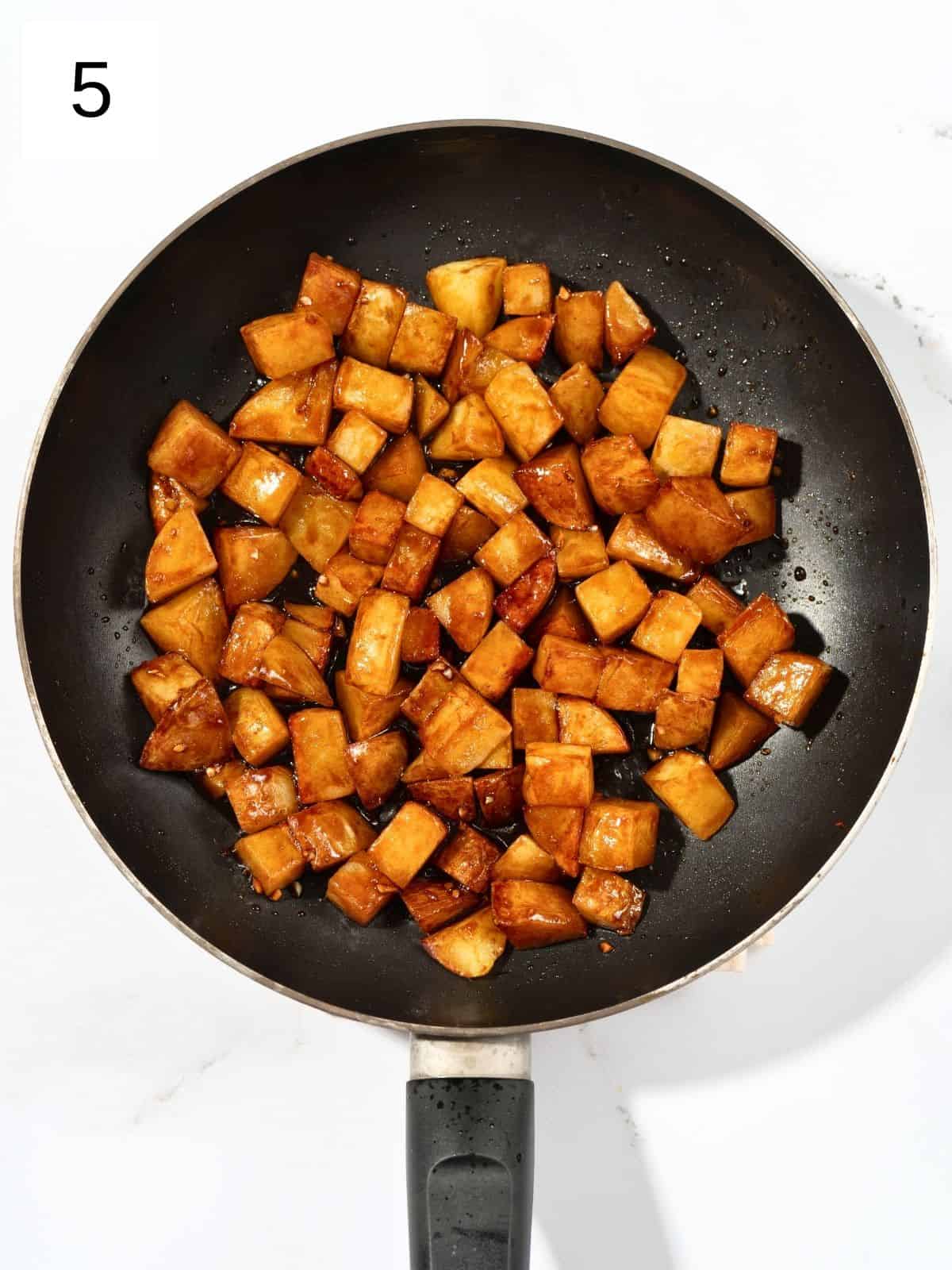 Potato cuts coated with gochujang and soy sauce mixture in a pan.