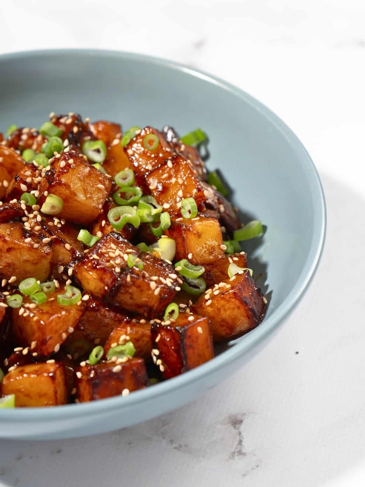 A bowl of gochujang potatoes sprinkled with sesame seeds and spring onions.