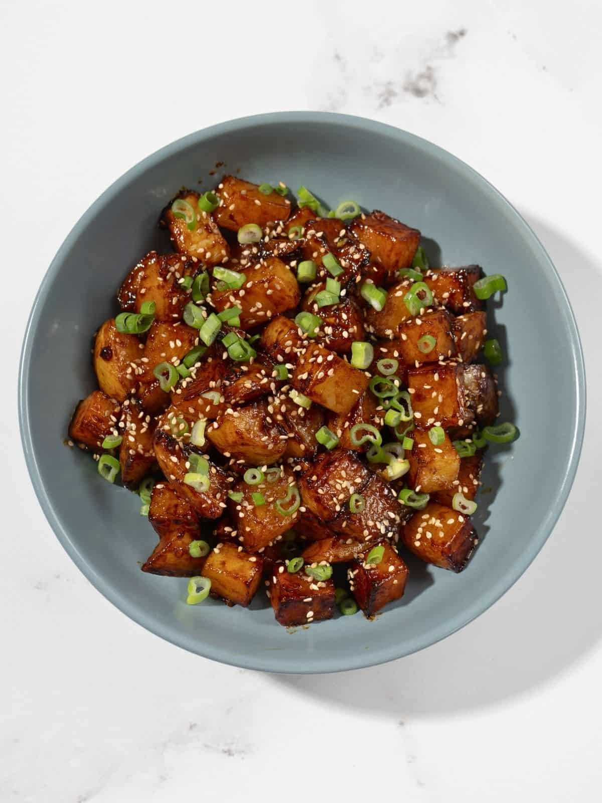 A bowl of gochujang potatoes sprinkled with sesame seeds and spring onions.