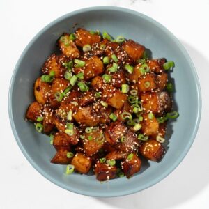 A bowl of gochujang potatoes sprinkled with sesame seeds and spring onions.