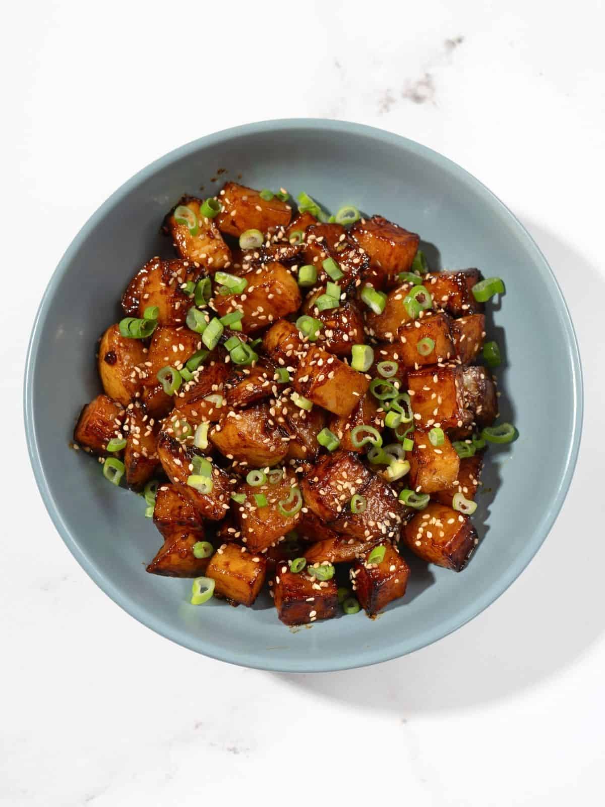 A bowl of gochujang potatoes sprinkled with sesame seeds and spring onions.