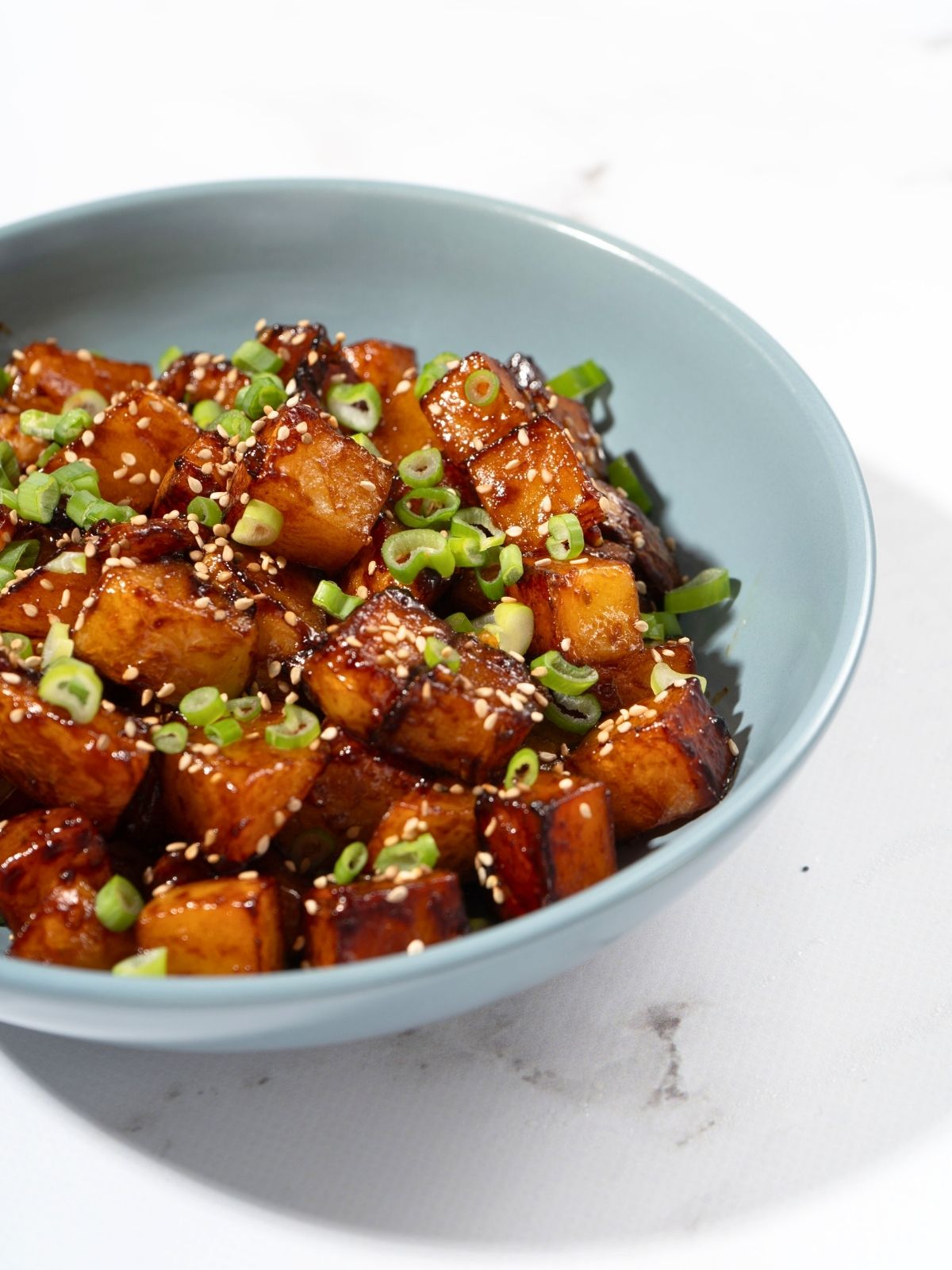 A bowl of gochujang potatoes sprinkled with sesame seeds and spring onions.