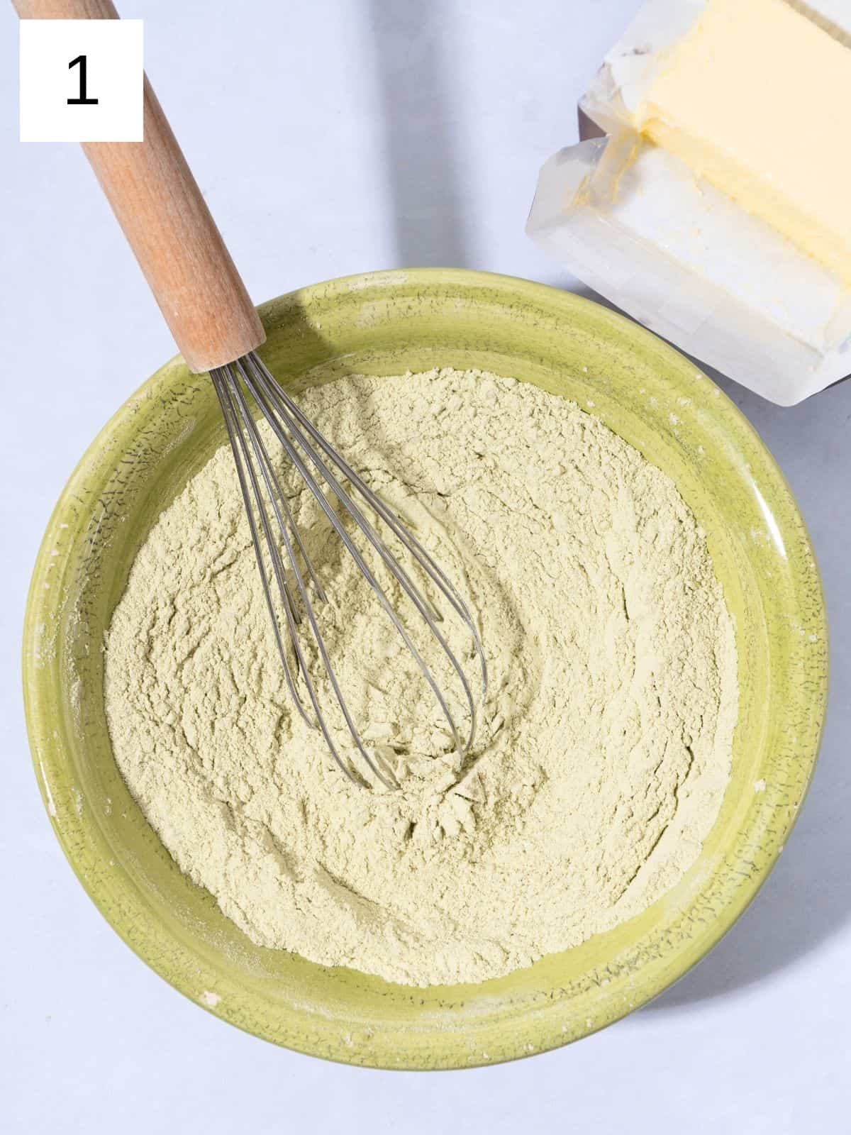 A bowl of flour and matcha powder mixed together with a whisk.