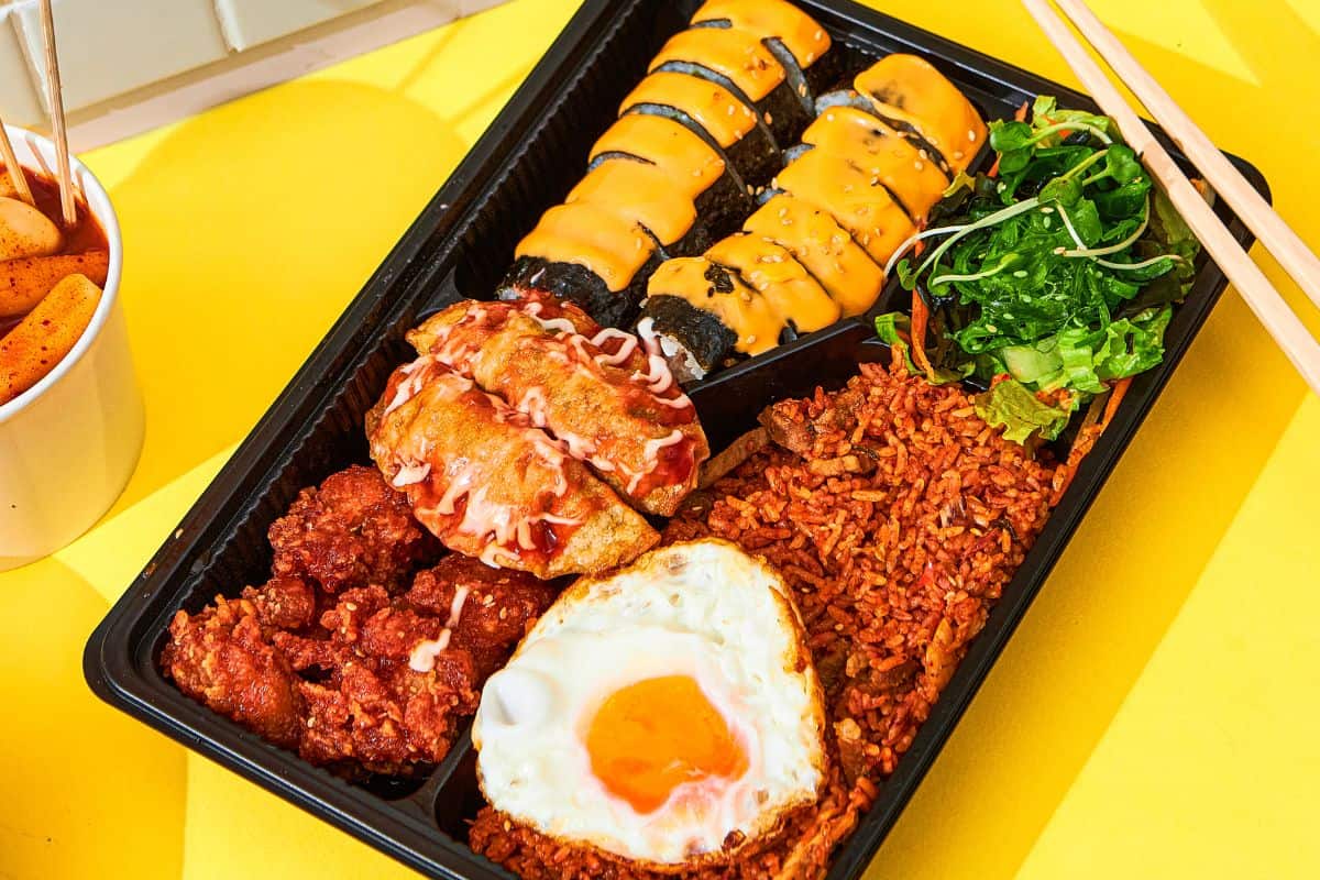 Overloaded dosirak with gimbap, kimchi fries rice, mandu, chicken pops, and some fresh vegetables.