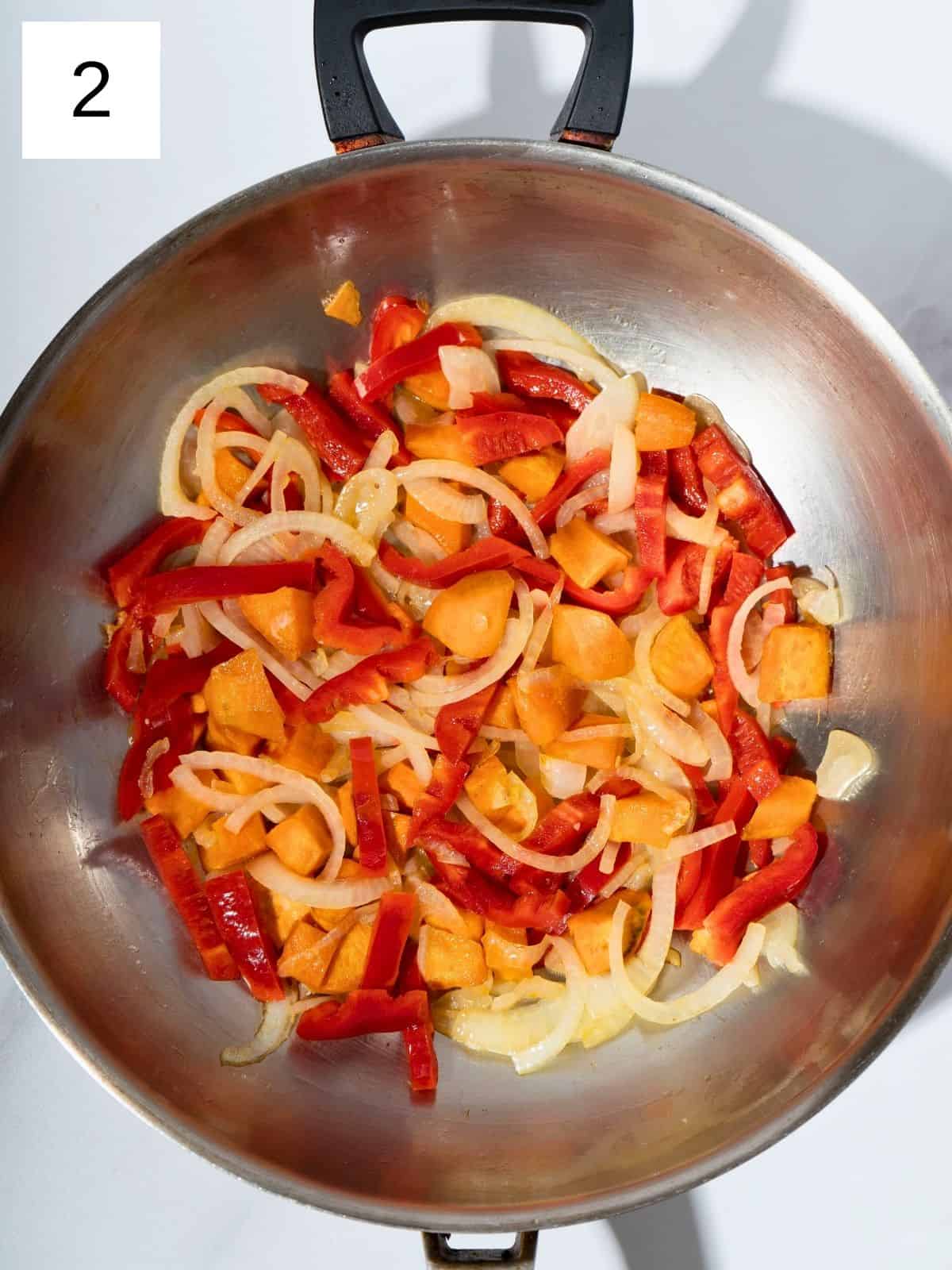 Diced sweet potatoes, sliced onions, carrots, and bell peppers sautéing in a large wok, sizzling in sesame oil and creating a vibrant, aromatic stir fry base.