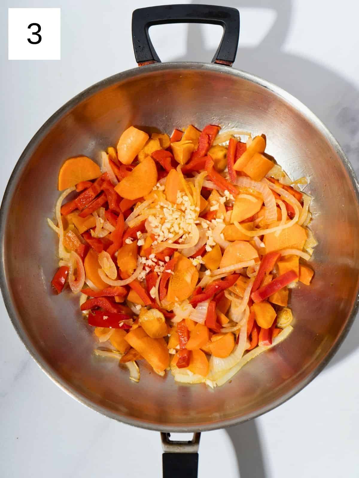 Diced sweet potatoes, sliced onions, carrots, and bell peppers sautéing in a large wok, with minced garlic and ginger added for extra flavor, creating a colorful and aromatic stir fry.