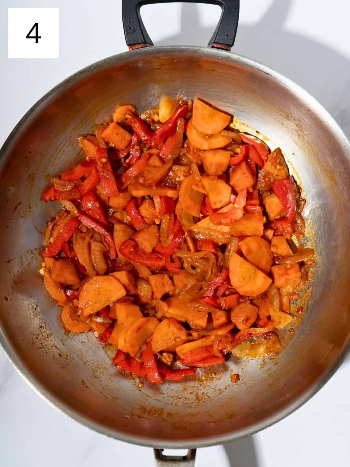 Diced sweet potatoes, sliced onions, carrots, and bell peppers sautéing in a large wok, with minced garlic, ginger, gochujang, soy sauce, and salt added, creating a flavorful and vibrant stir fry.