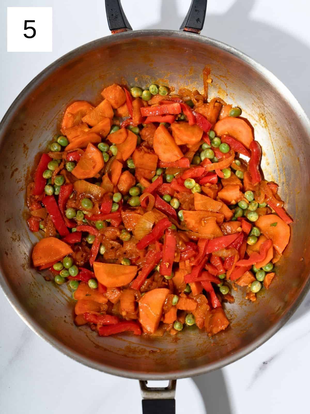 Diced sweet potatoes, sliced onions, carrots, and bell peppers sautéing in a large wok, with minced garlic, ginger, gochujang, soy sauce, salt, and frozen peas added, creating a colorful and flavorful stir fry.
