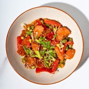 Colorful gochujang stir fry vegetables served in a plate, featuring diced sweet potatoes, sliced bell peppers, carrots, and green onions, garnished with sesame seeds.