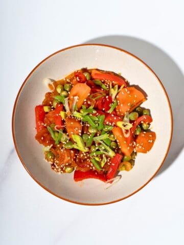 Colorful gochujang stir fry vegetables served in a plate, featuring diced sweet potatoes, sliced bell peppers, carrots, and green onions, garnished with sesame seeds.