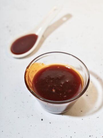 A small glass and a spoonful of honey gochujang sauce.
