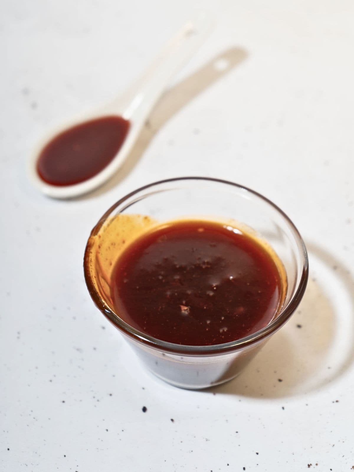 A small glass and a spoonful of honey gochujang sauce.