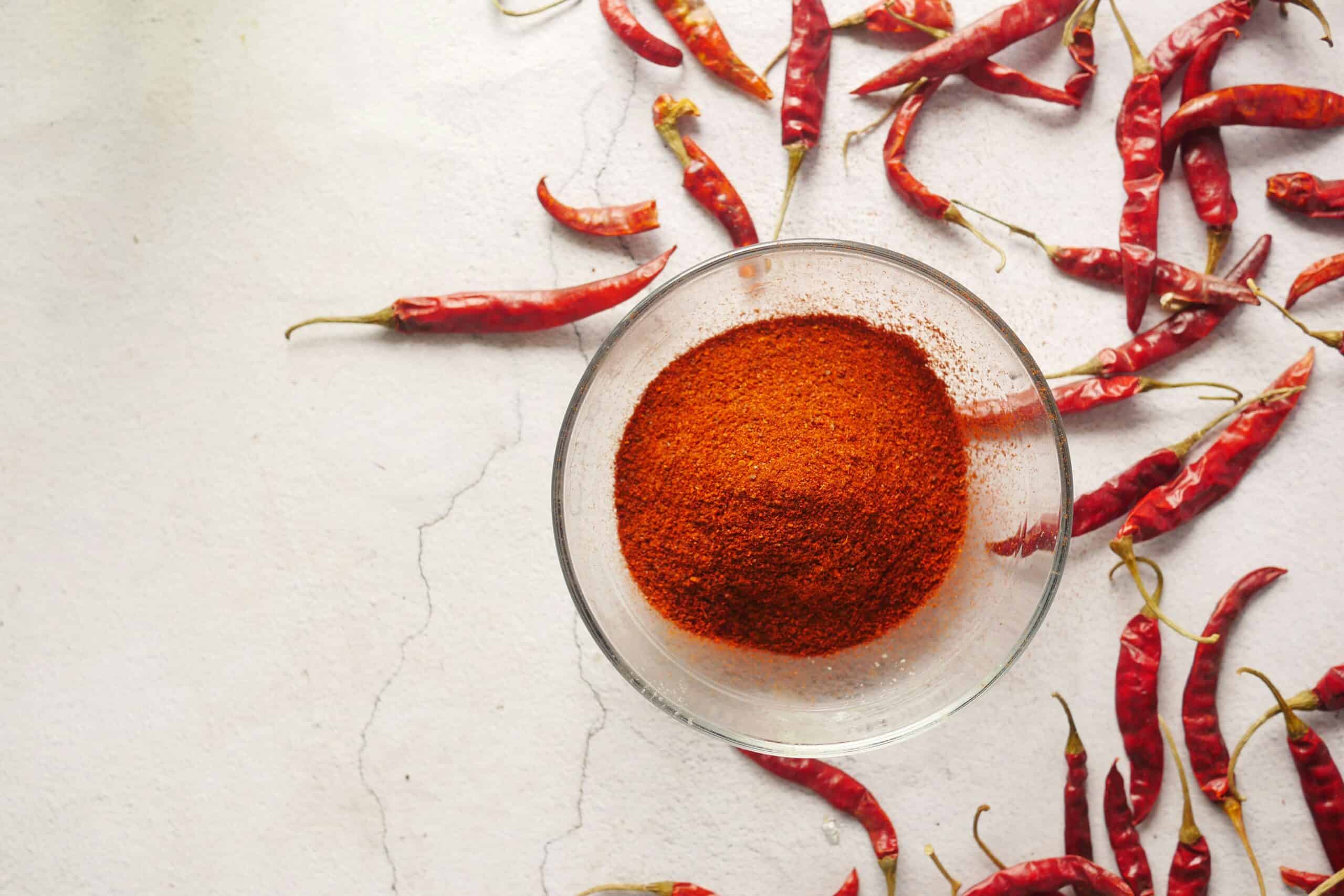 Chili powder in a bowl surrounded by chilies. 