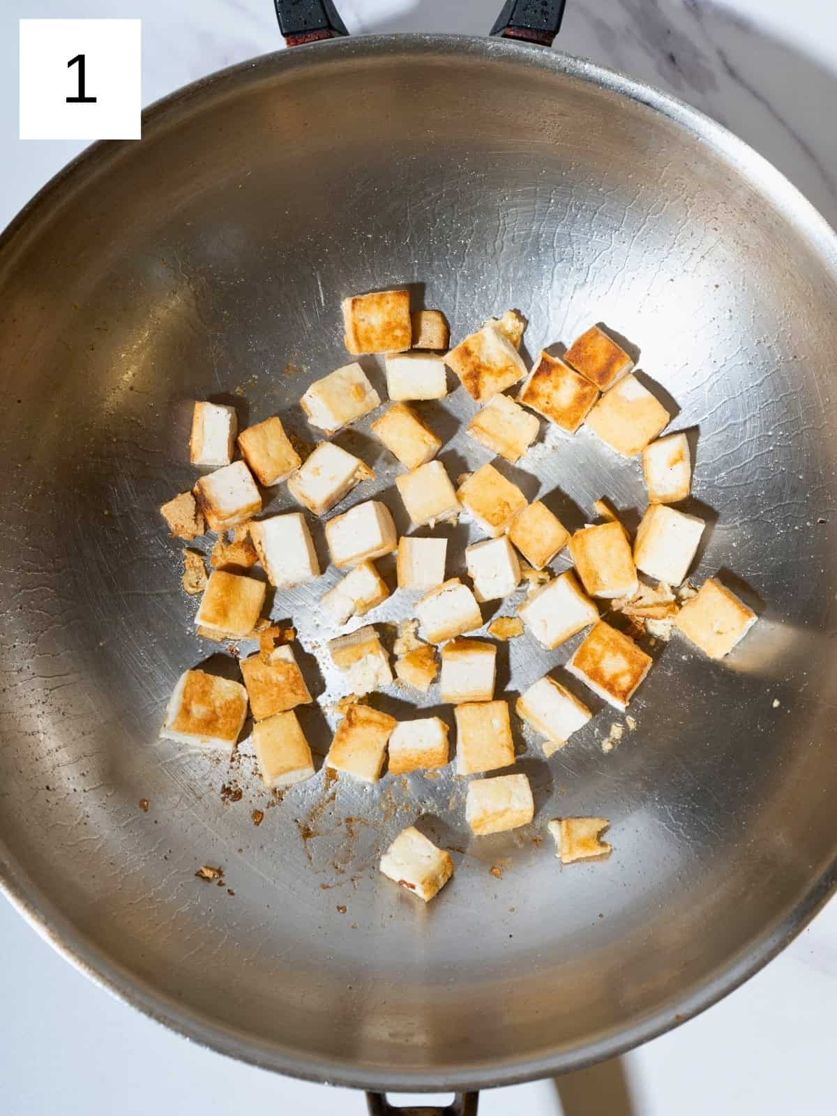 Golden-brown tofu cubes sizzling in a skillet, showcasing their crispy texture and appetizing color as they cook.