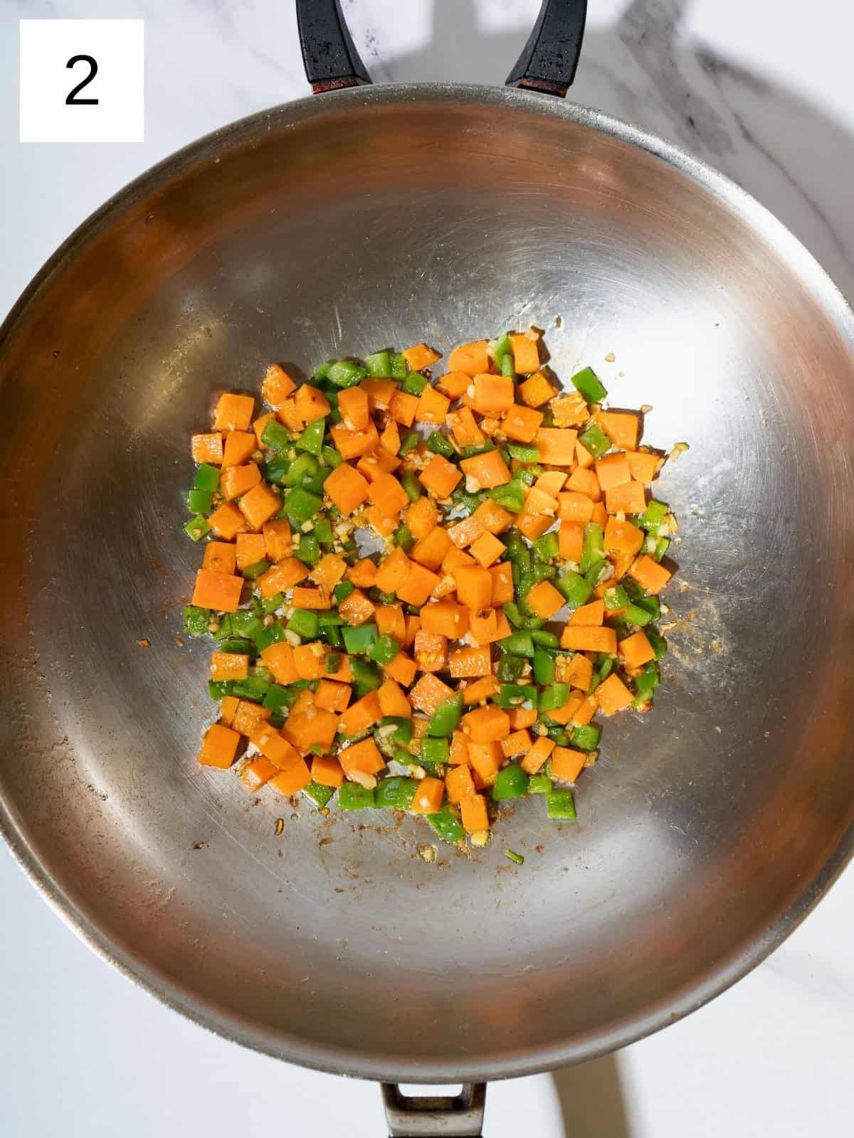 Colorful diced carrots and bell peppers sautéing in a skillet with minced garlic and ginger.
