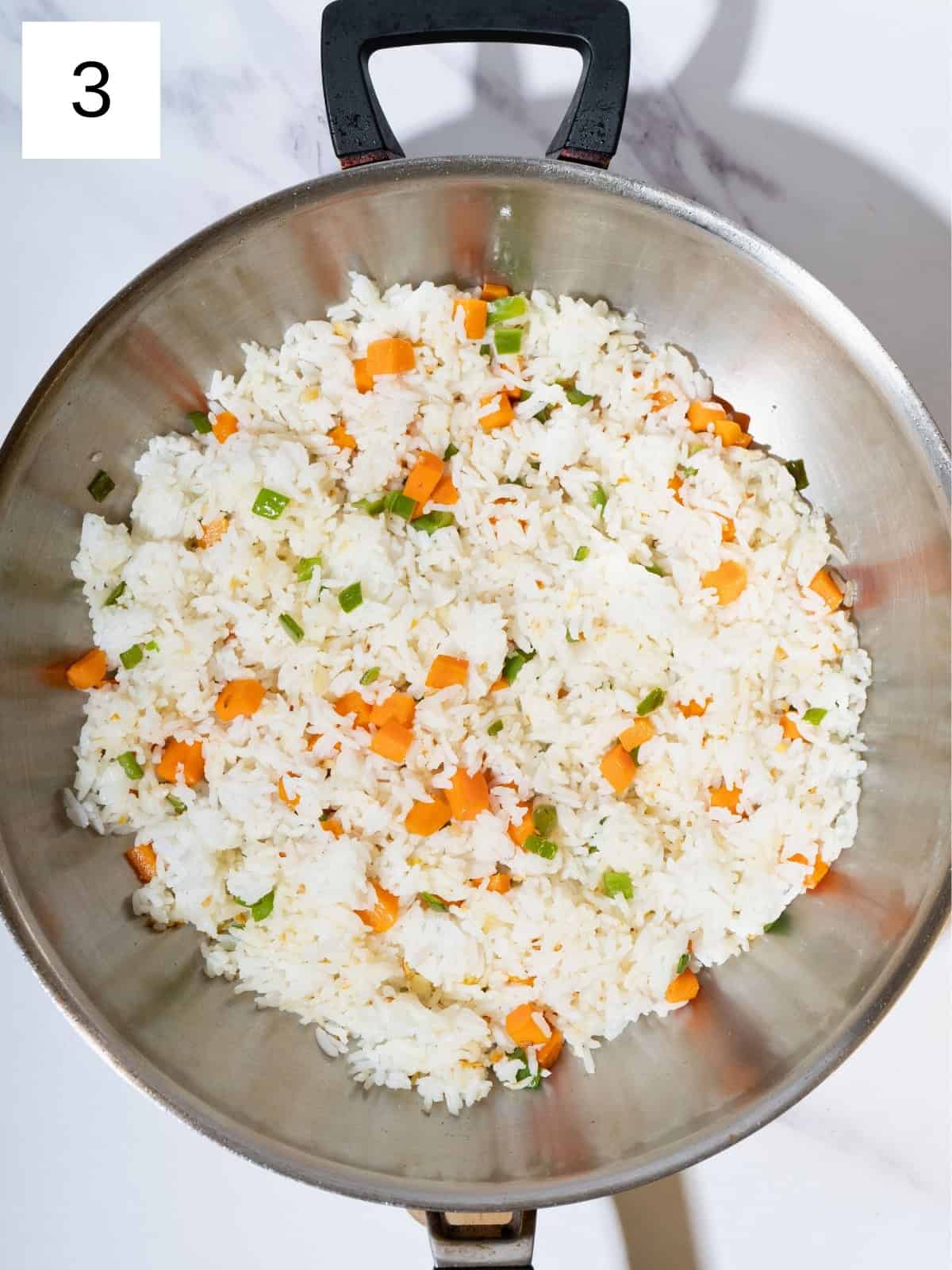 Cooked rice mixed with cubed carrots and bell peppers in a skillet.