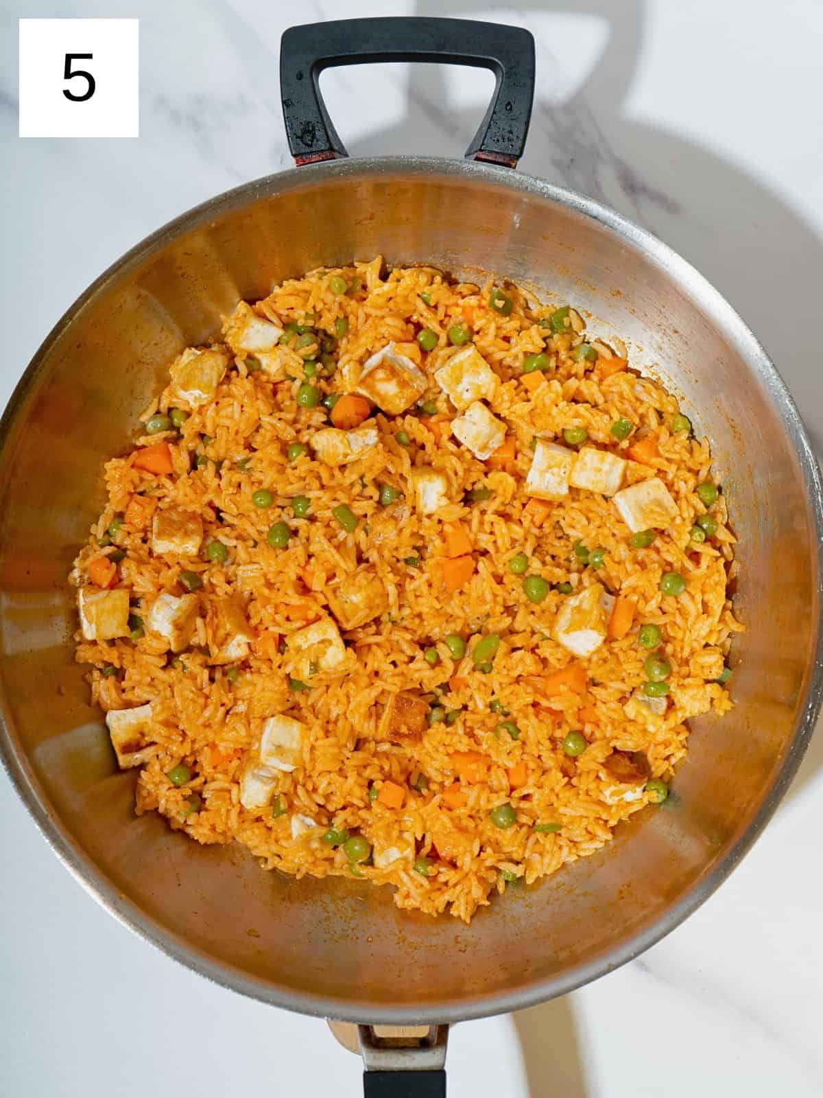 A colorful mixture of rice, vegetables, gochujang, peas, and cubed tofu squares sizzling in a skillet, showcasing a delicious and nutritious one-pan meal.