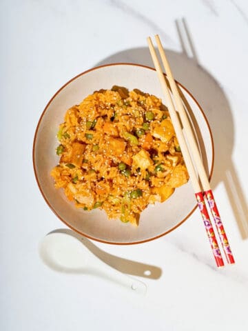 Delicious gochujang fried rice topped with colorful vegetables and cubed tofu, served on a plate, showcasing its vibrant colors and savory appeal.