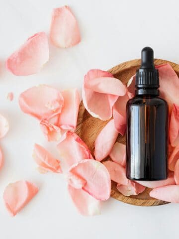 An amber-colored dropper bottle use for skincare surrounded by pink fower petals.