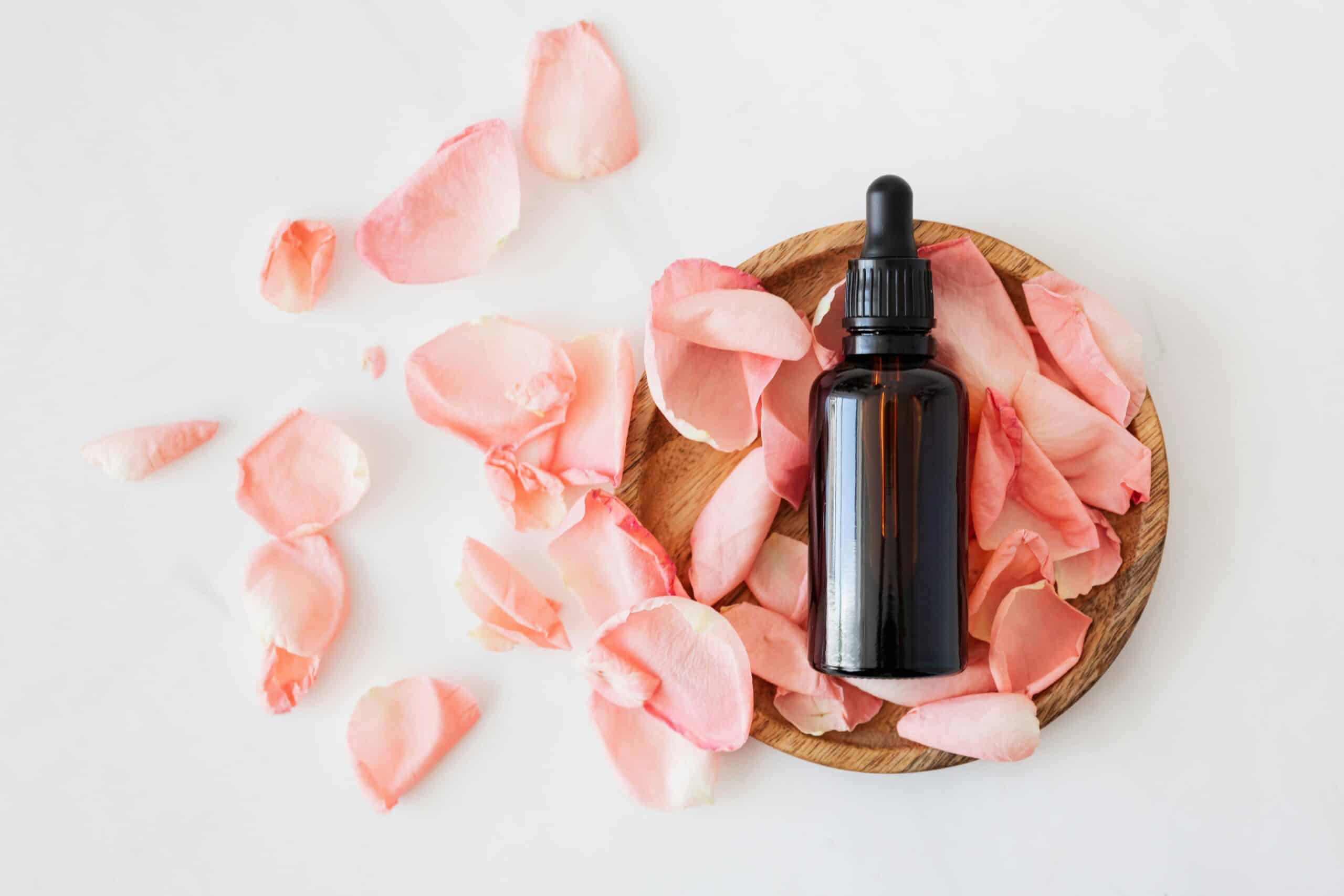 An amber-colored dropper bottle use for skincare surrounded by pink fower petals.