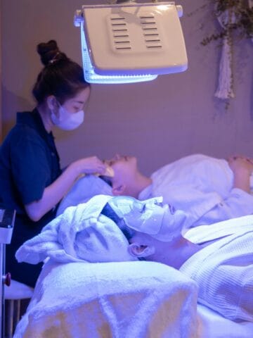 Person receiving a facial treatment under an LED light therapy machine in a spa setting, highlighting K-beauty’s use of technology in skincare.
