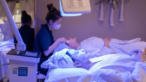Person receiving a facial treatment under an LED light therapy machine in a spa setting, highlighting K-beauty’s use of technology in skincare.