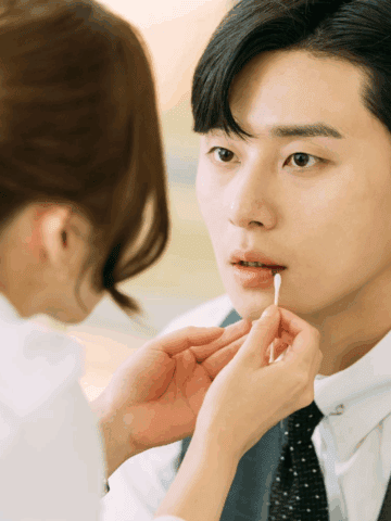 Close-up of Secretary Kim gently applying lip balm to Vice Chairman Lee Young-joon as he sits still, wide-eyed and stunned in his suit.