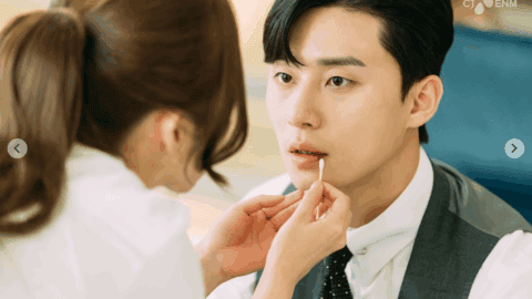 Close-up of Secretary Kim gently applying lip balm to Vice Chairman Lee Young-joon as he sits still, wide-eyed and stunned in his suit.