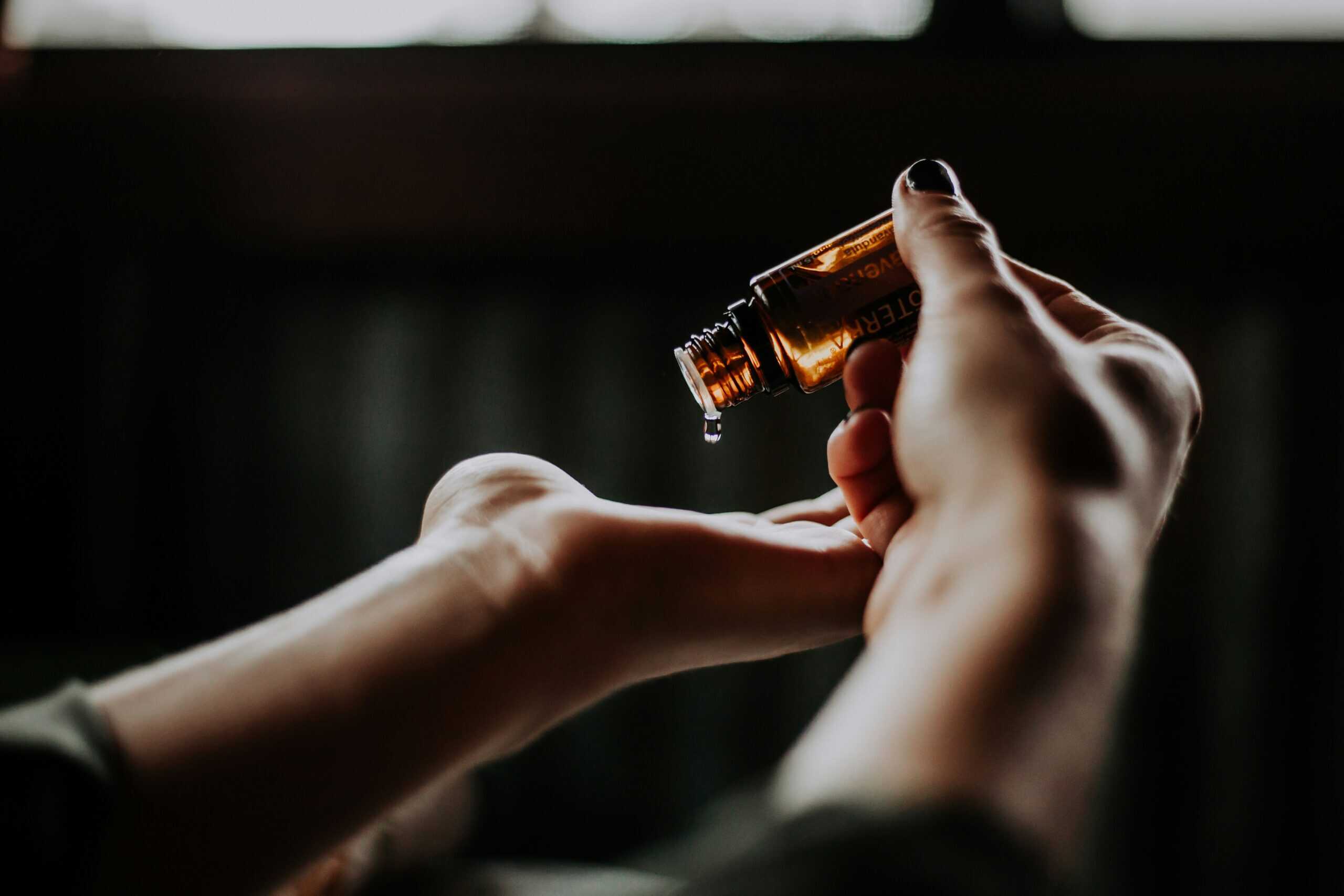 Close-up of hands dispensing skincare oil from a brown bottle in a softly lit room, highlighting a minimal and calm aesthetic.
