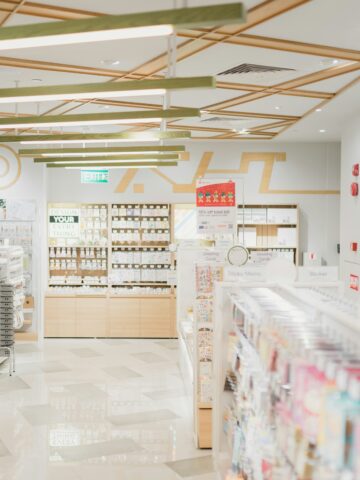 Wide-angle view of a well-lit modern drugstore, filled with skincare and personal care products on neatly organized shelves.