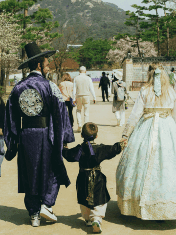 A family wearing traditional Korean hanbok walking hand-in-hand through a historical palace garden during Chuseok.