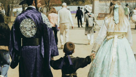 A family wearing traditional Korean hanbok walking hand-in-hand through a historical palace garden during Chuseok.