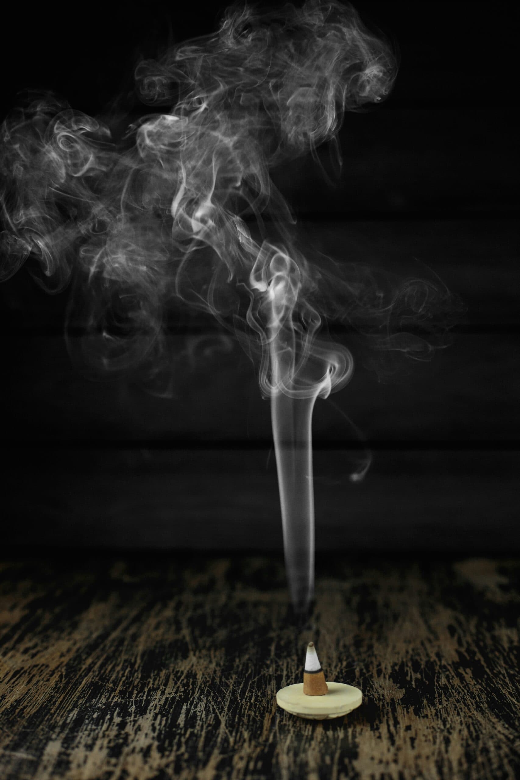 Smoking incense stick creating smoke art, black background, Asian spiritual ritual, aromatic incense, serene atmosphere.