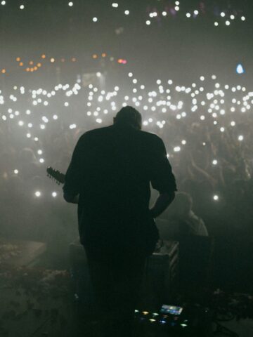 A man performing on stage during a concert in Seoul, Korea, with an audience using smartphone lights.