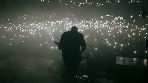 A man performing on stage during a concert in Seoul, Korea, with an audience using smartphone lights.